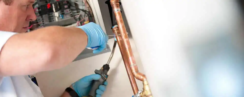 Water heater repair technician testing copper pipe connections and controls in Duluth, MN